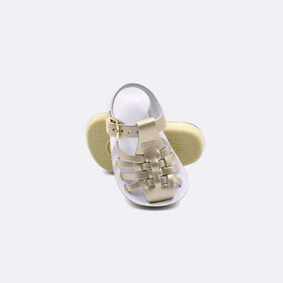 Two baby sized 4200 Sailor style sandals with gold straps and white insoles.  One standing with the sole facing the camera. The second is laying diagonally over the top left edge of the sole.
