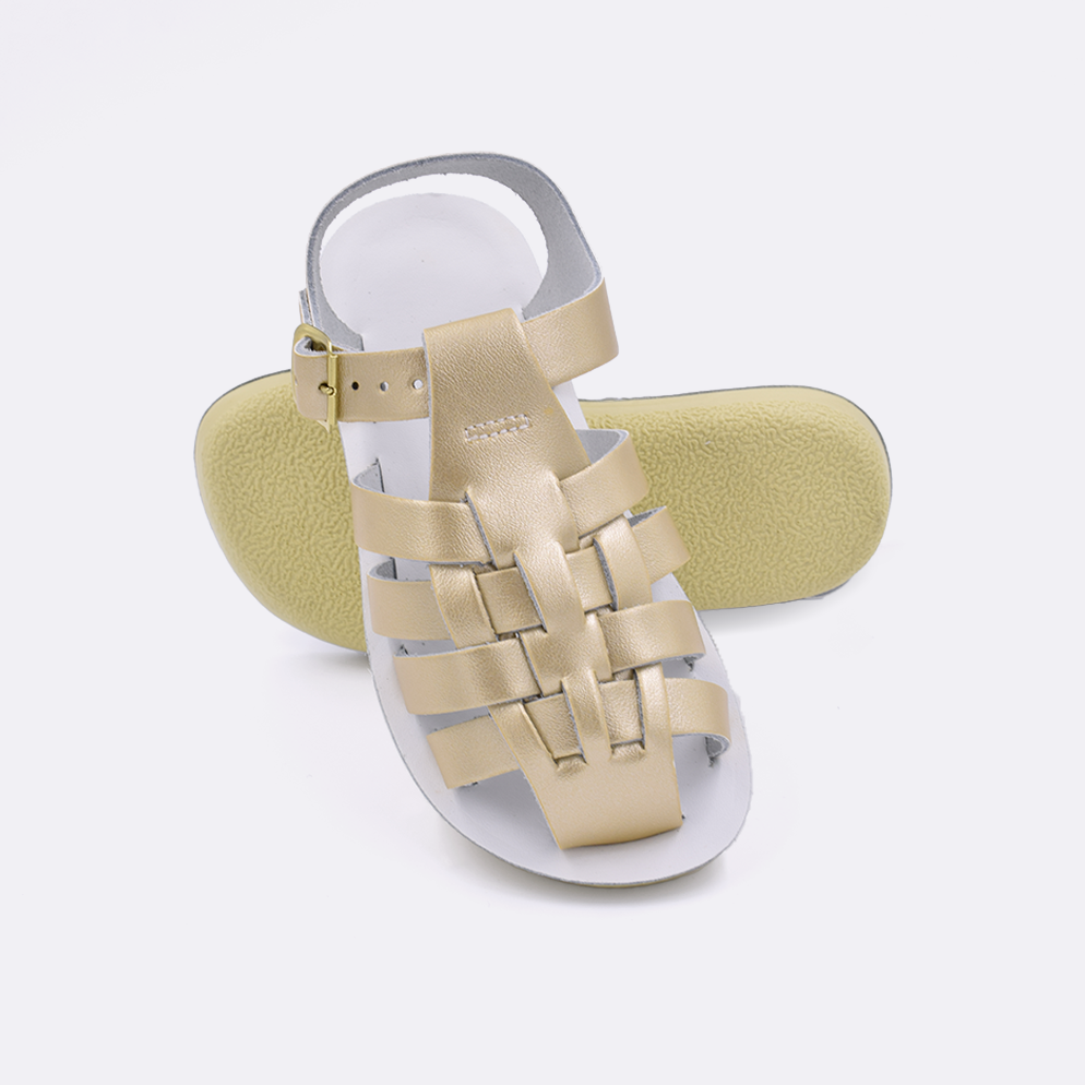 Two little kid sized 4200 Sailor style sandals with gold straps and white insoles.  One standing with the sole facing the camera. The second is laying diagonally over the top left edge of the sole.