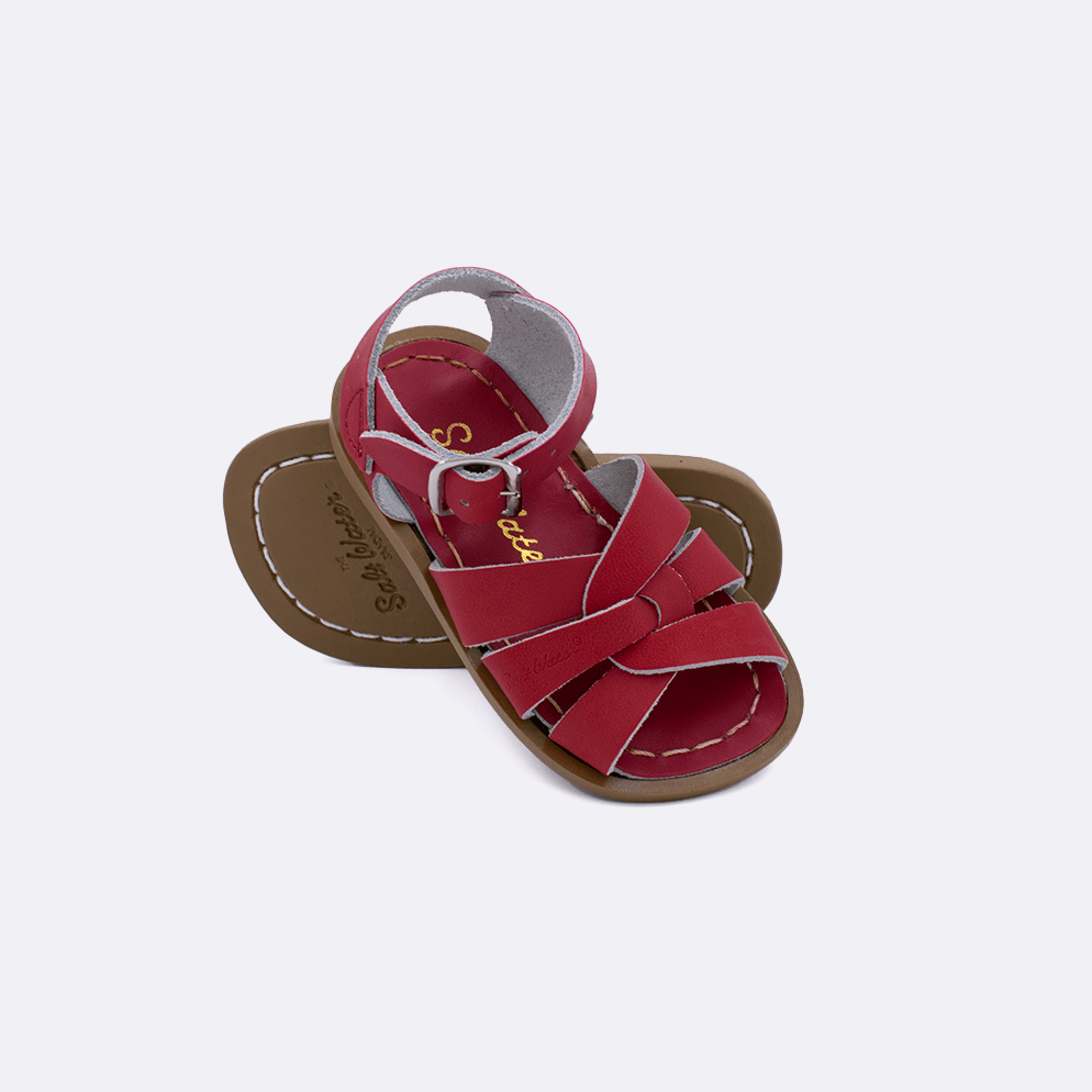 Two baby size 800 Original style sandals color red.  One standing with the sole facing the camera. The second is laying diagonally over the top left edge of the sole.