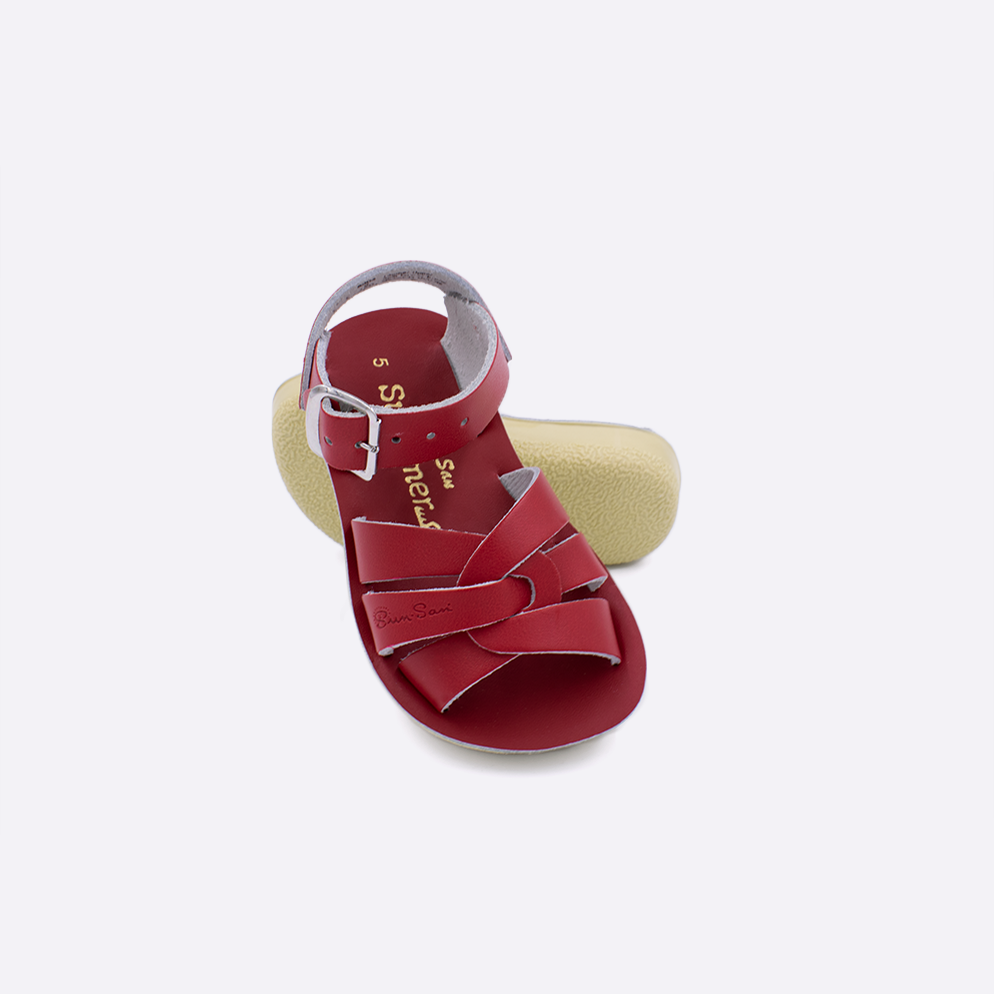 Two toddler sized 8000 Swimmer style sandals with red straps and red insoles.  One standing with the sole facing the camera. The second is laying diagonally over the top left edge of the sole.