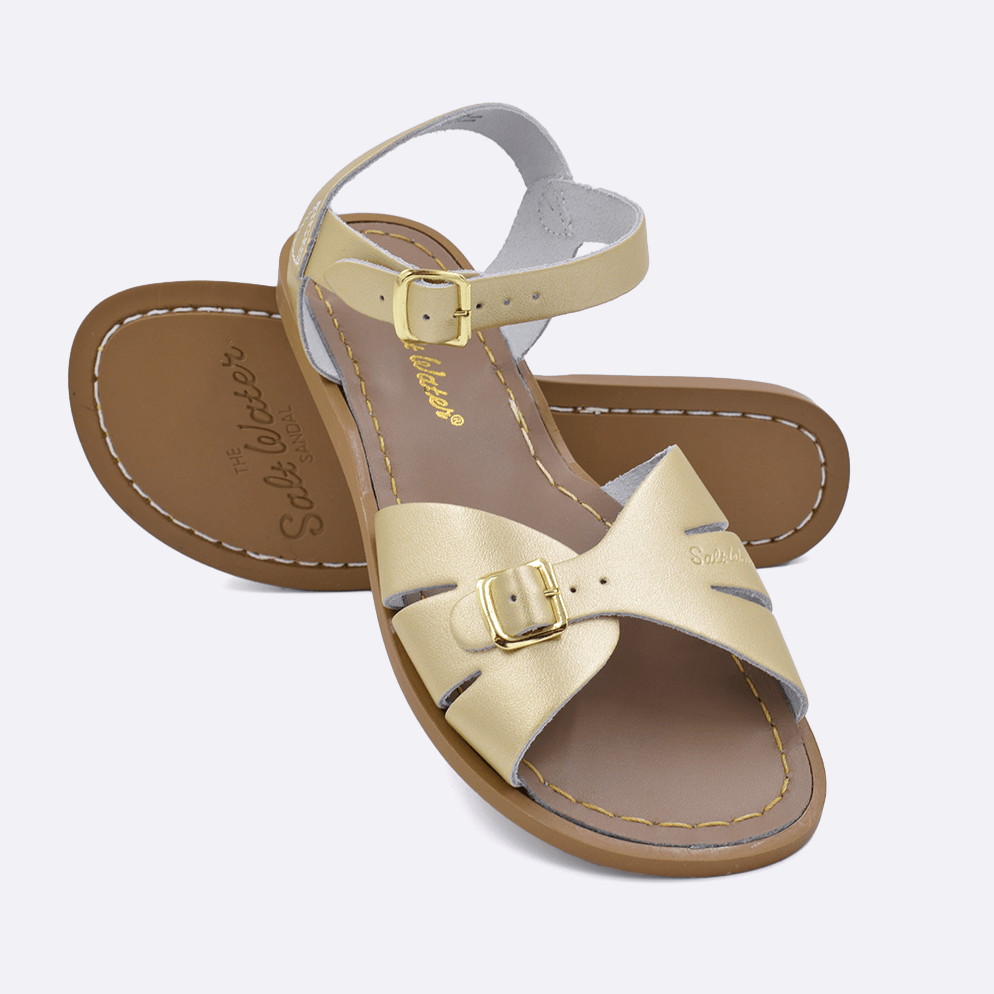 Two 900 Classic style sandals color gold.  One standing with the sole facing the camera. The second is laying diagonally over the top left edge of the sole.	Adult Size.