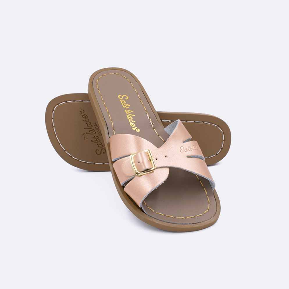 Two 9900 Classic Slide style sandals color rose gold.  One standing with the sole facing the camera. The second is laying diagonally over the top left edge of the sole.	Little Kid Size.