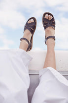 A close up photo of an adult wearing our brown originals has their feet up on the side of a white boat facing the sky.