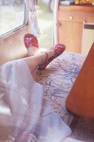 A close up picture of an adults legs crossed wearing a light blue and white striped dress. They are laying down in a van with their legs crossed wearing red salt water original sandals on blue and yellow flowered deat.