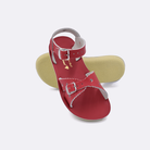 Two little kid sized 1400 Sweetheart style sandals with red straps and red insoles.  One standing with the sole facing the camera. The second is laying diagonally over the top left edge of the sole.