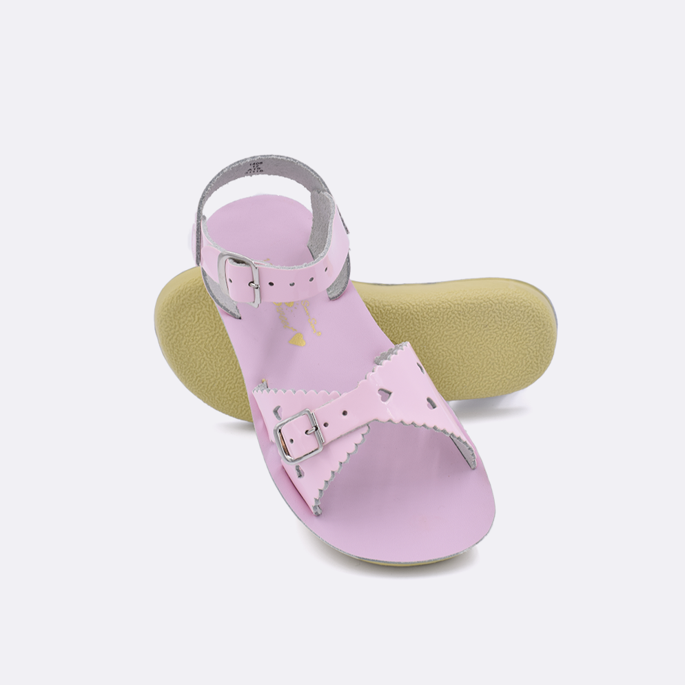 Two little kid sized 1400 Sweetheart style sandals with shiny pink straps and shiny pink insoles.  One standing with the sole facing the camera. The second is laying diagonally over the top left edge of the sole.