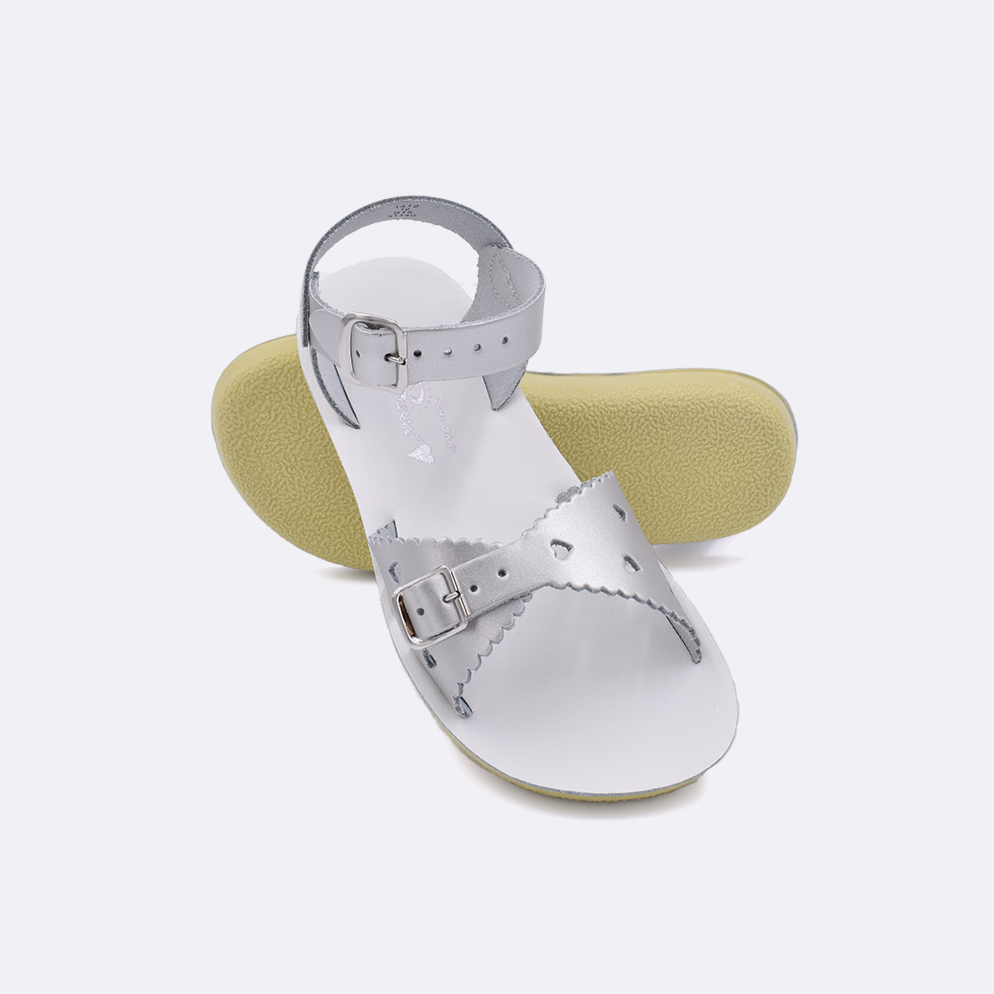 Two little kid sized 1400 Sweetheart style sandals with silver straps and white insoles.  One standing with the sole facing the camera. The second is laying diagonally over the top left edge of the sole.