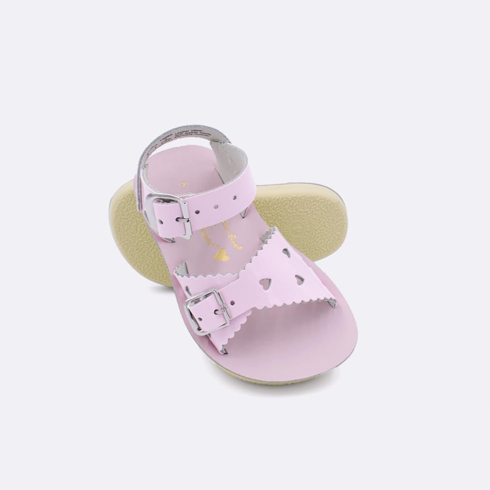 Two toddler sized 1400 Sweetheart style sandals with shiny pink straps and shiny pink insoles.  One standing with the sole facing the camera. The second is laying diagonally over the top left edge of the sole.