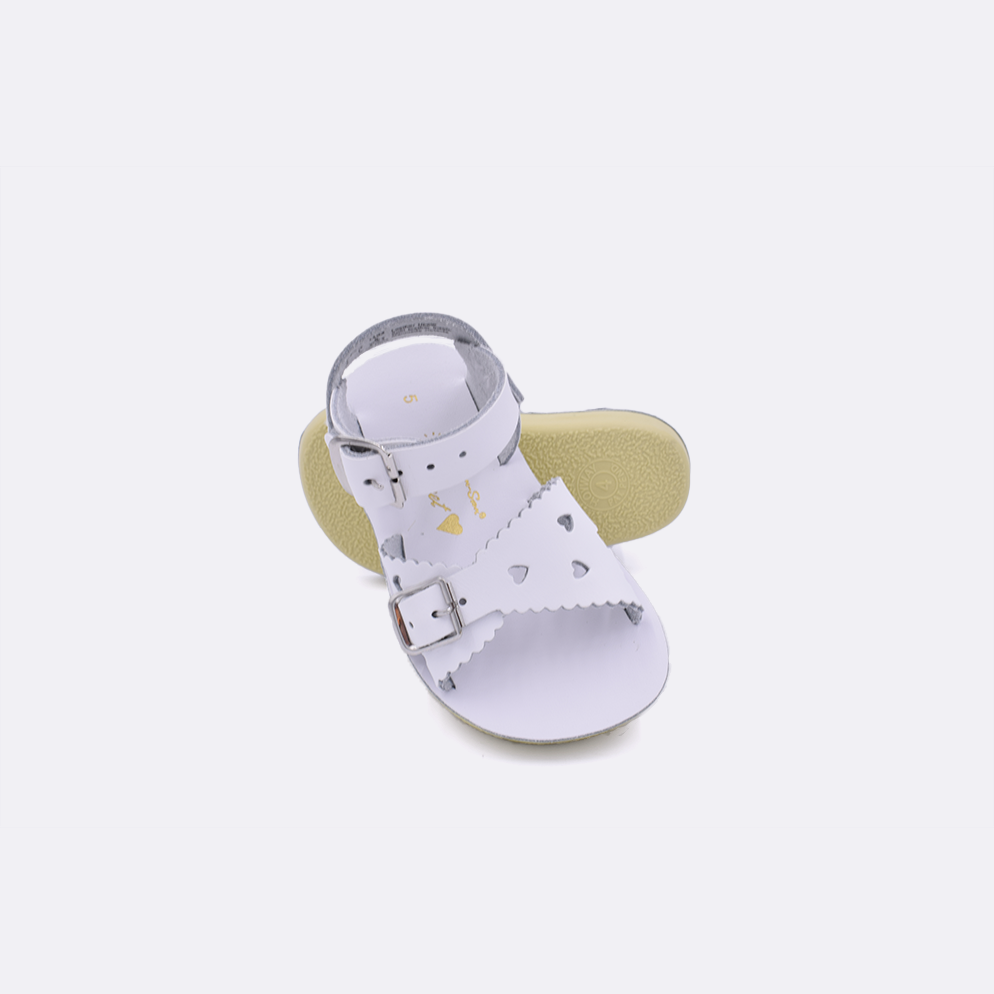 Two toddler sized 1400 Sweetheart style sandals with white straps and white insoles.  One standing with the sole facing the camera. The second is laying diagonally over the top left edge of the sole.
