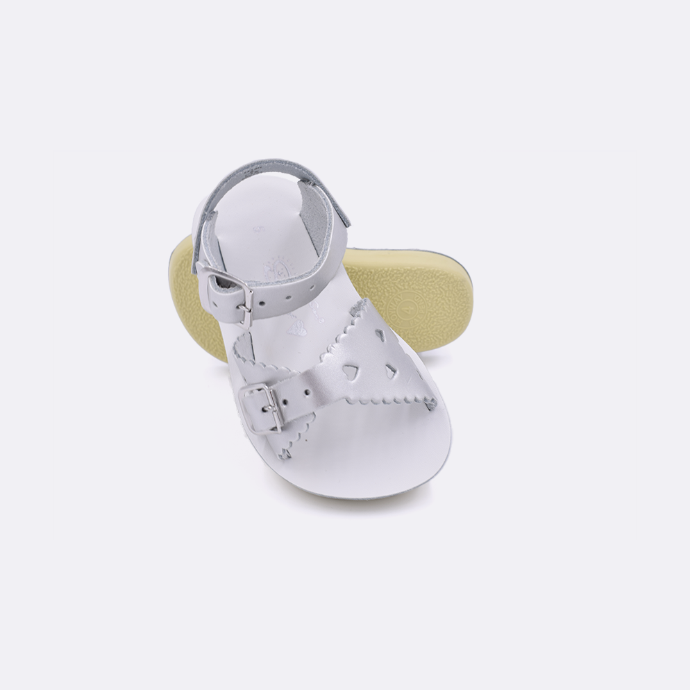Two toddler sized 1400 Sweetheart style sandals with silver straps and white insoles.  One standing with the sole facing the camera. The second is laying diagonally over the top left edge of the sole.