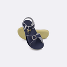 Two toddler sized 1700 Surfer style sandals with navy straps and navy insoles.  One standing with the sole facing the camera. The second is laying diagonally over the top left edge of the sole.