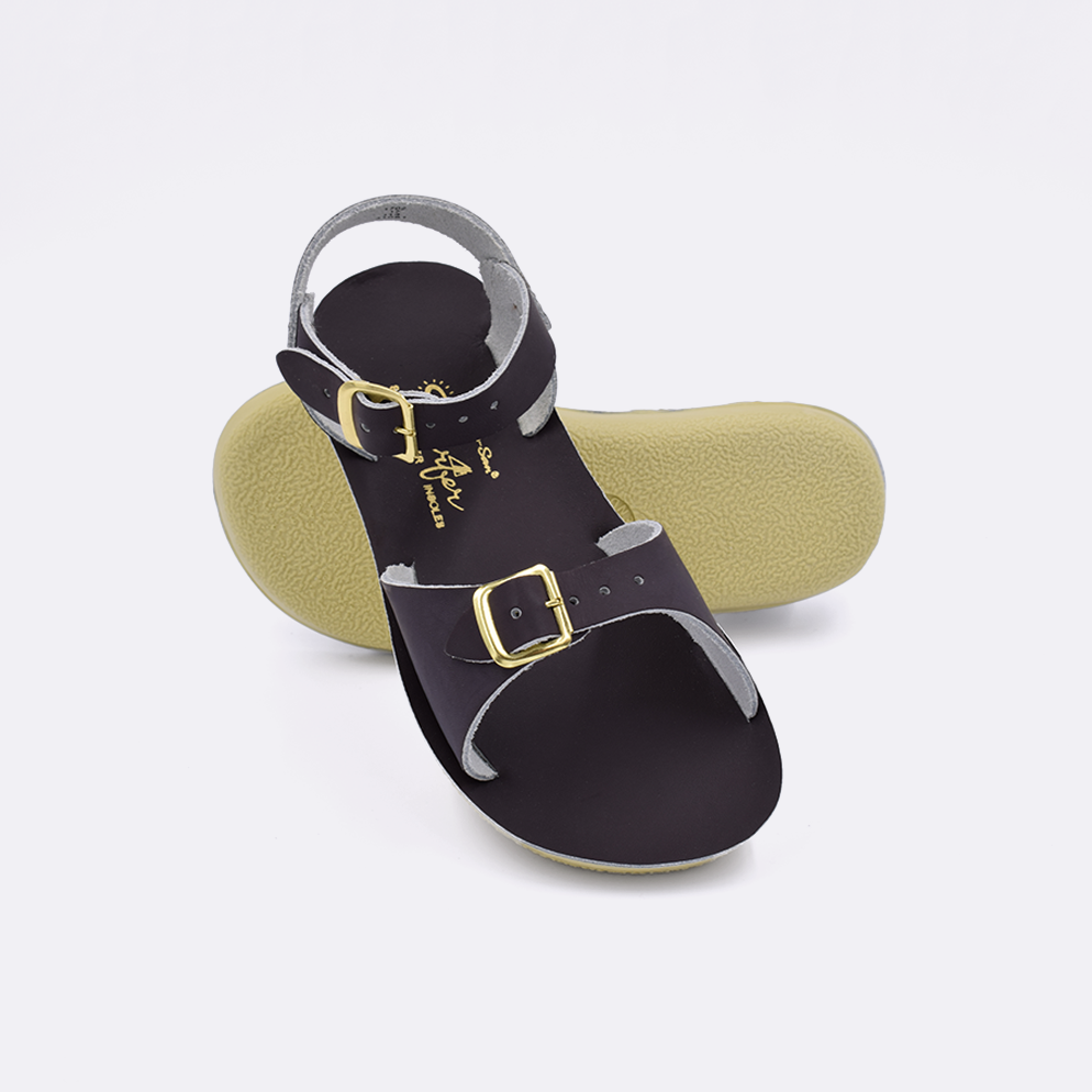 Two little kid sized 1700 Surfer style sandals with brown straps and brown insoles.  One standing with the sole facing the camera. The second is laying diagonally over the top left edge of the sole.