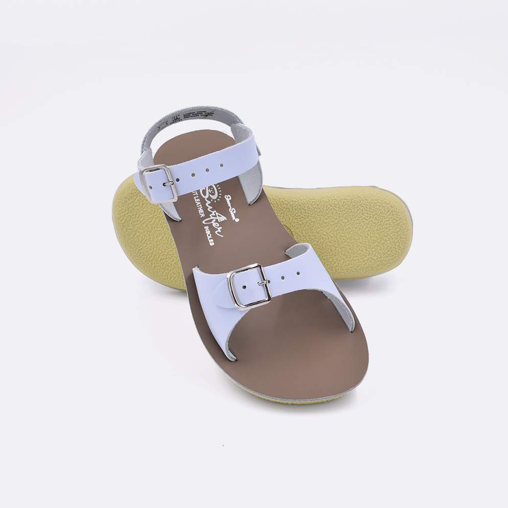 Two little kid sized 1700 Surfer style sandals with light blue straps and beige insoles.  One standing with the sole facing the camera. The second is laying diagonally over the top left edge of the sole.
