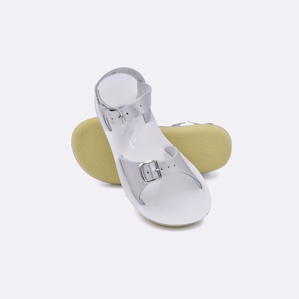 Two little kid sized 1700 Surfer style sandals with silver straps and white insoles.  One standing with the sole facing the camera. The second is laying diagonally over the top left edge of the sole.