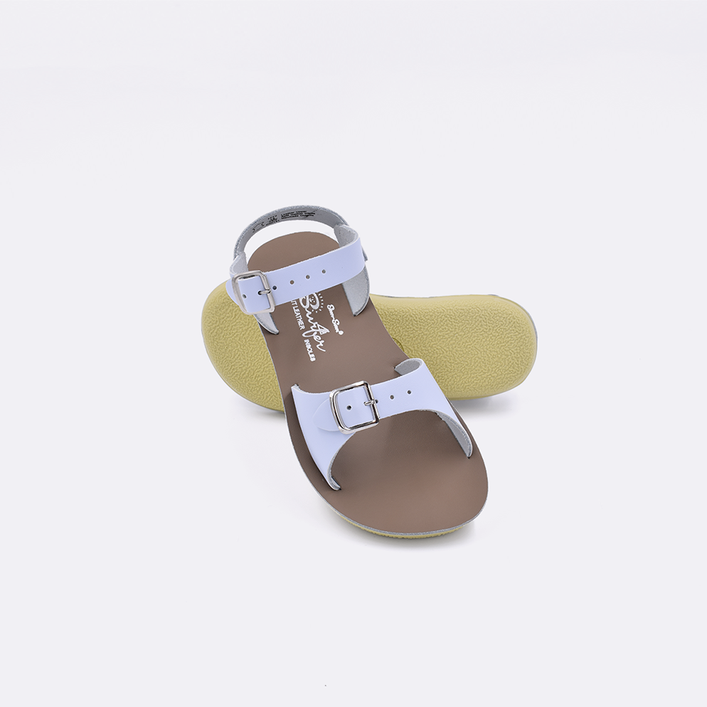 Two toddler sized 1700 Surfer style sandals with light blue straps and beige insoles.  One standing with the sole facing the camera. The second is laying diagonally over the top left edge of the sole.