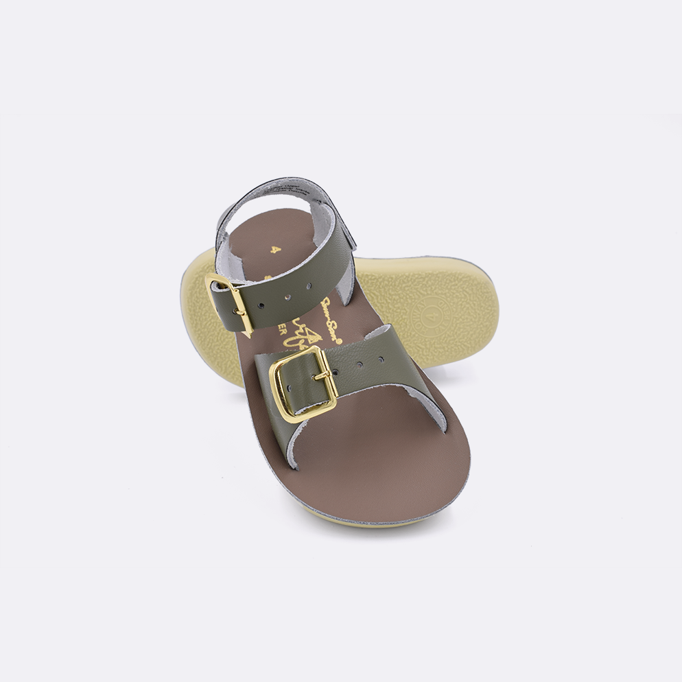 Two baby sized 1700 Surfer style sandals with olive straps and beige insoles.  One standing with the sole facing the camera. The second is laying diagonally over the top left edge of the sole.