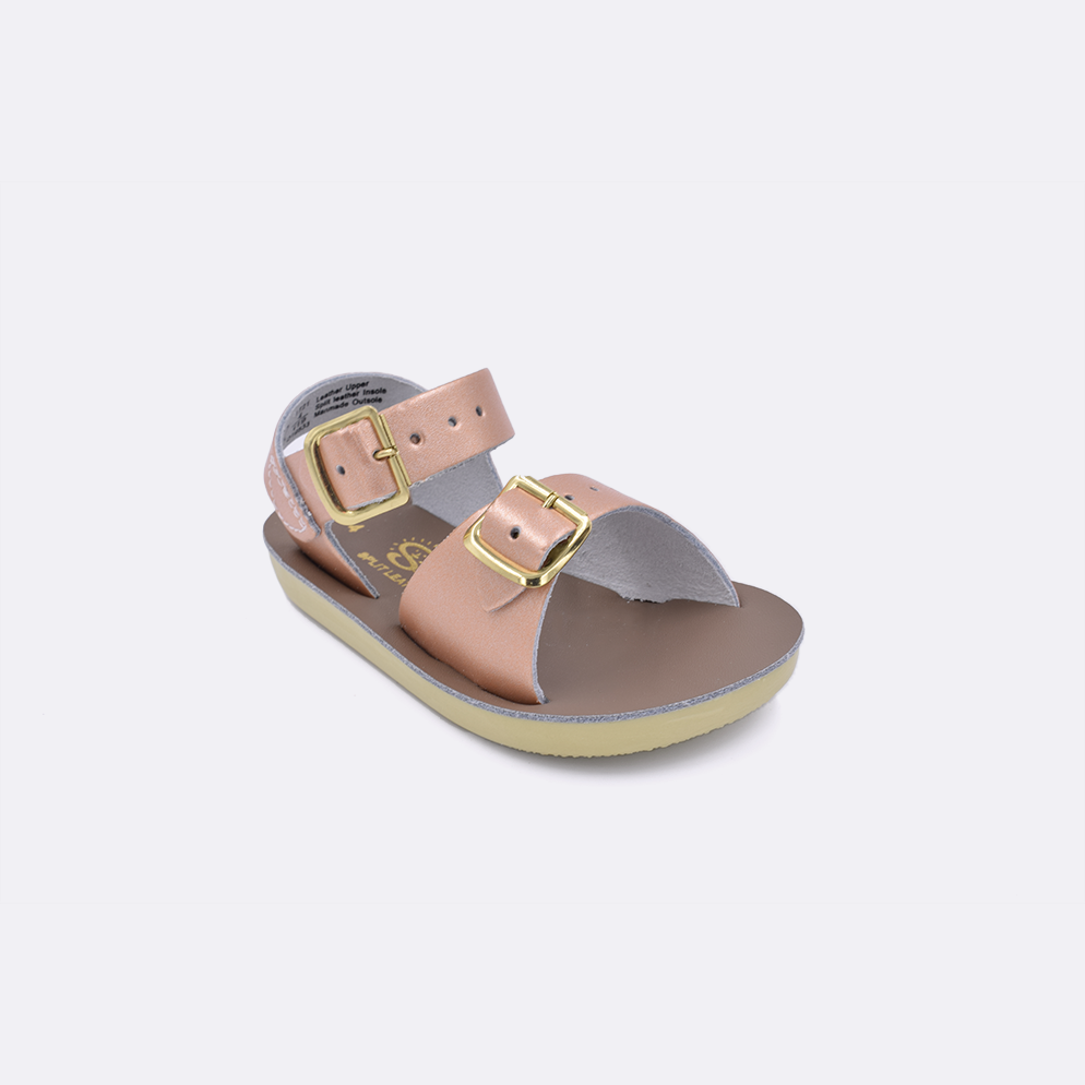 One baby sized 1700 Surfer style sandal with rose gold straps and a beige insole. Facing left to right diagonally. 