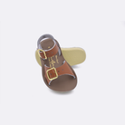 Two baby sized 1700 Surfer style sandals with tan straps and beige insoles.  One standing with the sole facing the camera. The second is laying diagonally over the top left edge of the sole.