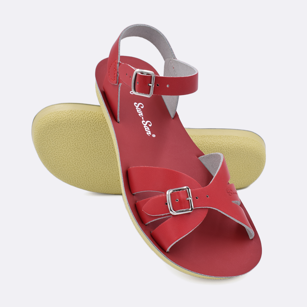 Two Women's sized 1900 Boardwalk style sandals with red straps and red insoles.  One standing with the sole facing the camera. The second is laying diagonally over the top left edge of the sole.