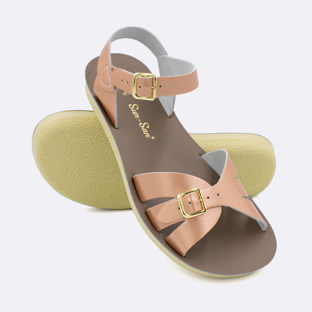 Two Women's sized 1900 Boardwalk style sandals with rose gold straps and beige insoles.  One standing with the sole facing the camera. The second is laying diagonally over the top left edge of the sole.