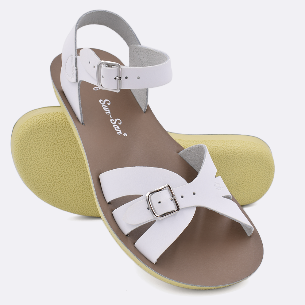 Two Women's sized 1900 Boardwalk style sandals with white straps and beige insoles.  One standing with the sole facing the camera. The second is laying diagonally over the top left edge of the sole.