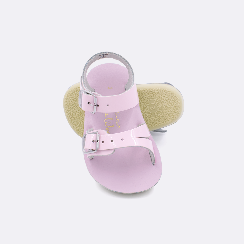 Two baby sized 2000 Sea Wee style sandals with shiny pink straps and shiny pink insoles.  One standing with the sole facing the camera. The second is laying diagonally over the top left edge of the sole.