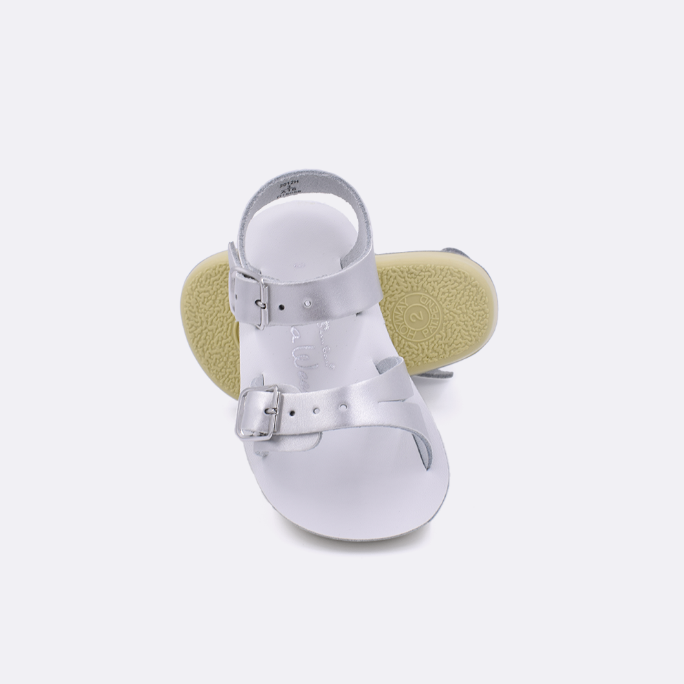 Two baby sized 2000 Sea Wee style sandals with silver straps and white insoles.  One standing with the sole facing the camera. The second is laying diagonally over the top left edge of the sole.