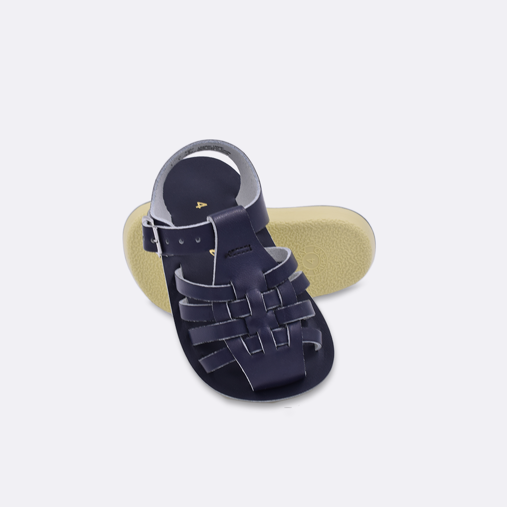 Two baby sized 4200 Sailor style sandals with navy straps and navy insoles.  One standing with the sole facing the camera. The second is laying diagonally over the top left edge of the sole.