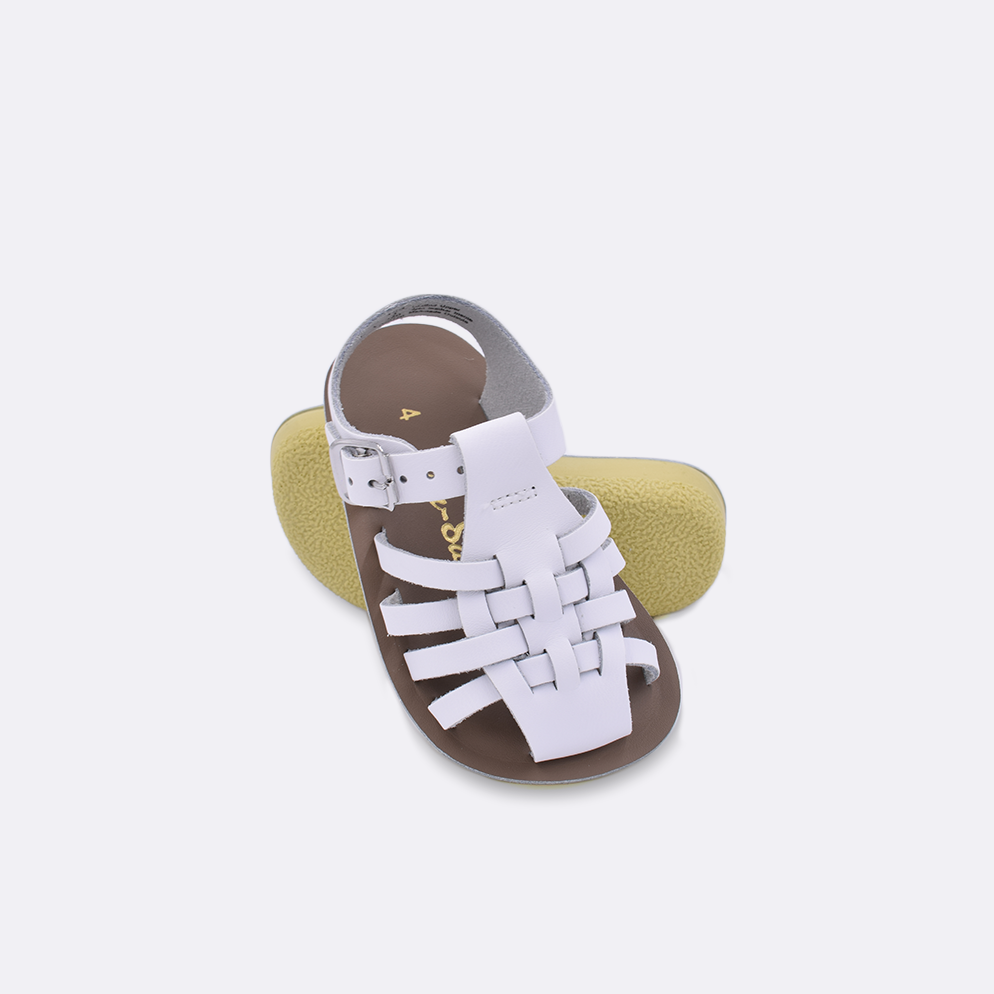 Two baby sized 4200 Sailor style sandals with white straps and beige insoles.  One standing with the sole facing the camera. The second is laying diagonally over the top left edge of the sole.