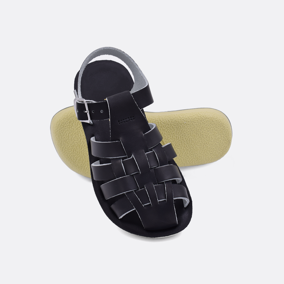 Two little kid sized 4200 Sailor style sandals with black straps and black insoles.  One standing with the sole facing the camera. The second is laying diagonally over the top left edge of the sole.