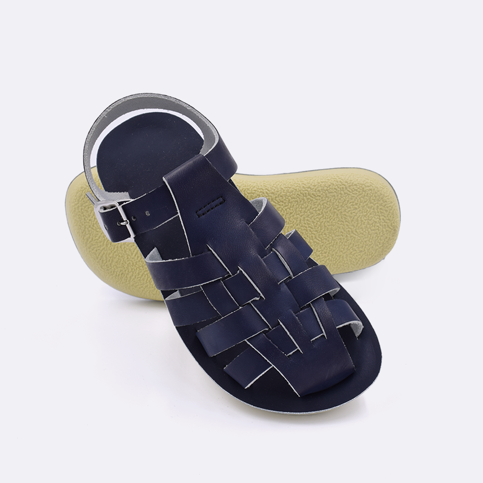Two little kid sized 4200 Sailor style sandals with navy straps and navy insoles.  One standing with the sole facing the camera. The second is laying diagonally over the top left edge of the sole.