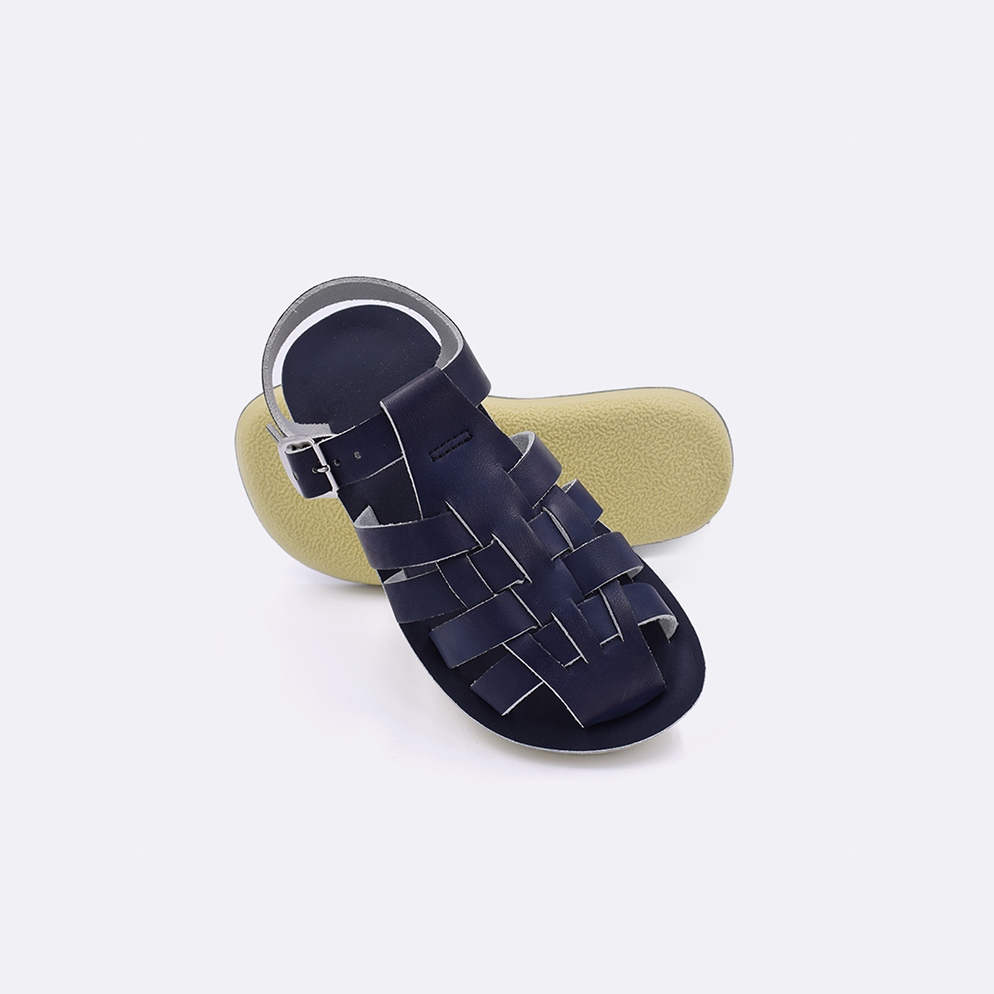 Two toddler sized 4200 Sailor style sandals with navy straps and navy insoles.  One standing with the sole facing the camera. The second is laying diagonally over the top left edge of the sole.