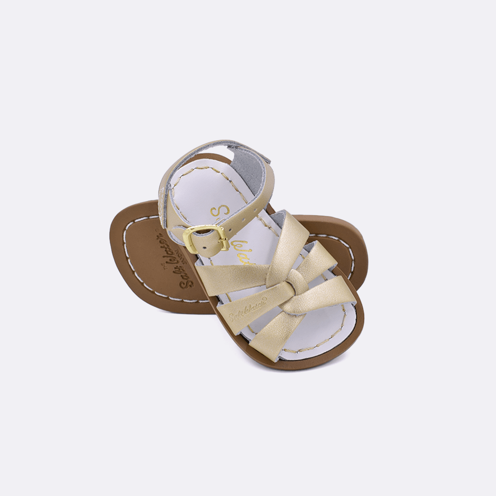 Two 800 Original style sandals color gold.  One standing with the sole facing the camera. The second is laying diagonally over the top left edge of the sole.	Baby size