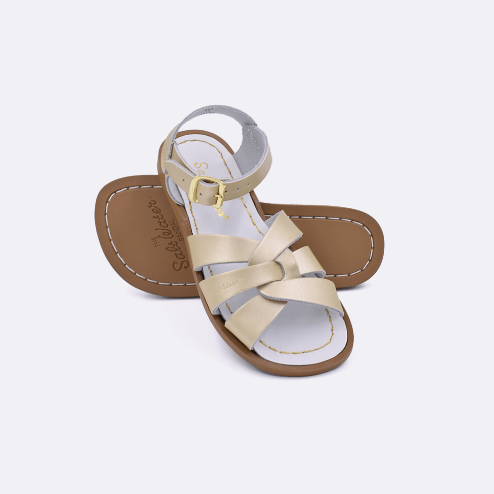 Two gold little kid sized 800 Original style sandals.  One standing with the sole facing the camera. The second is laying diagonally over the top left edge of the sole.