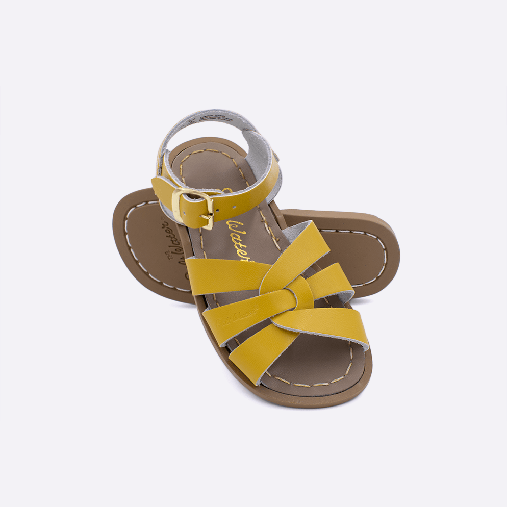 Two toddler sized 800 Original style sandals with mustard straps and beige insoles.  One standing with the sole facing the camera. The second is laying diagonally over the top left edge of the sole.