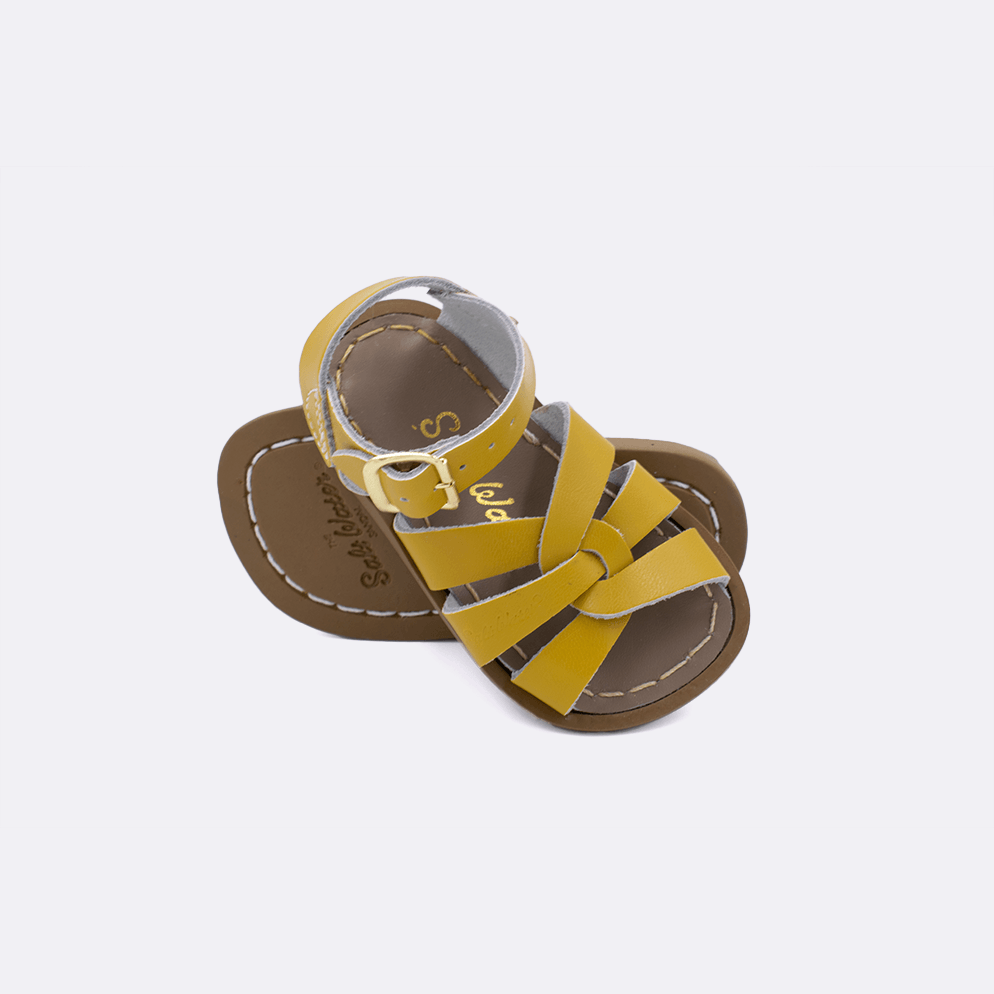 Two baby size 800 Original style sandals color mustard.  One standing with the sole facing the camera. The second is laying diagonally over the top left edge of the sole.