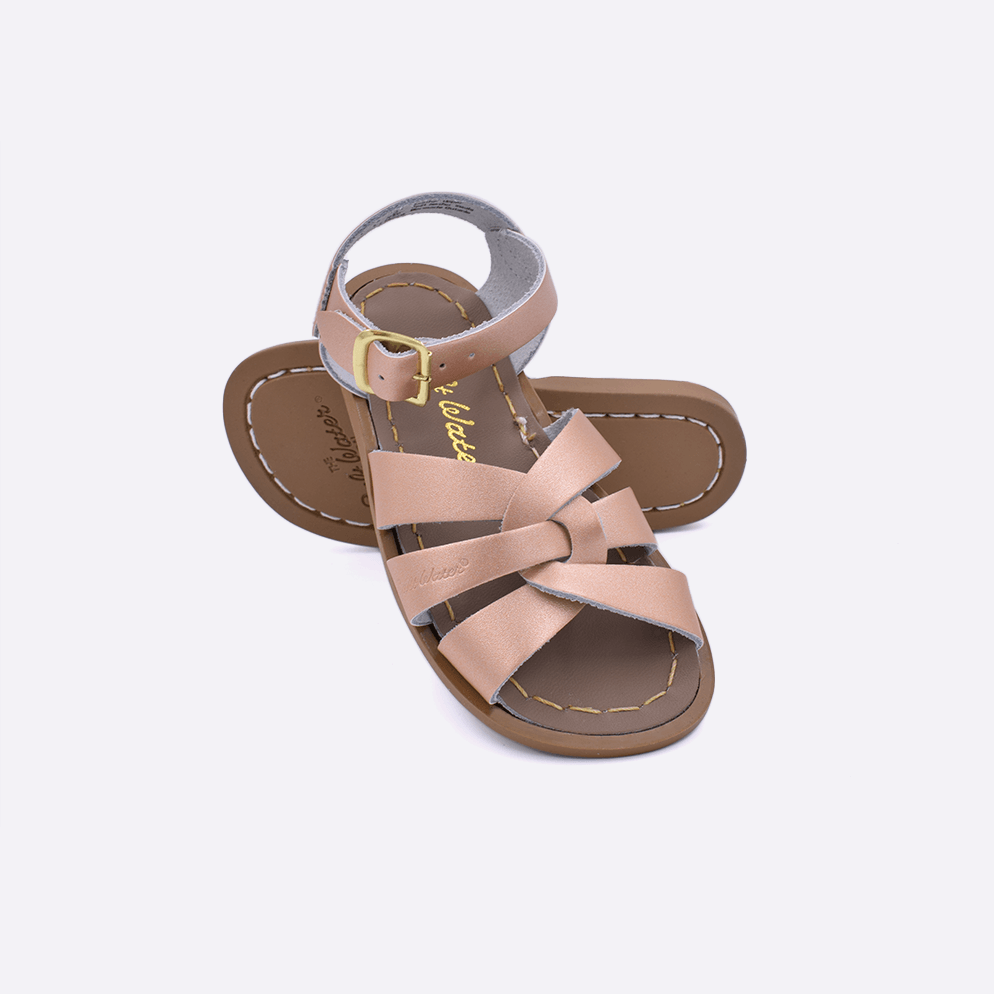 Two toddler sized 800 Original style sandals with rose gold straps and beige insoles.  One standing with the sole facing the camera. The second is laying diagonally over the top left edge of the sole.
