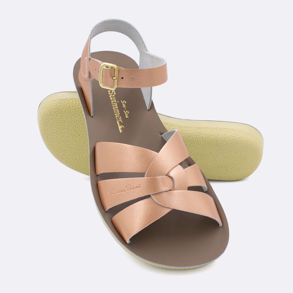 Two women's sized 8000 Swimmer style sandals with rose gold straps and beige insoles.  One standing with the sole facing the camera. The second is laying diagonally over the top left edge of the sole.