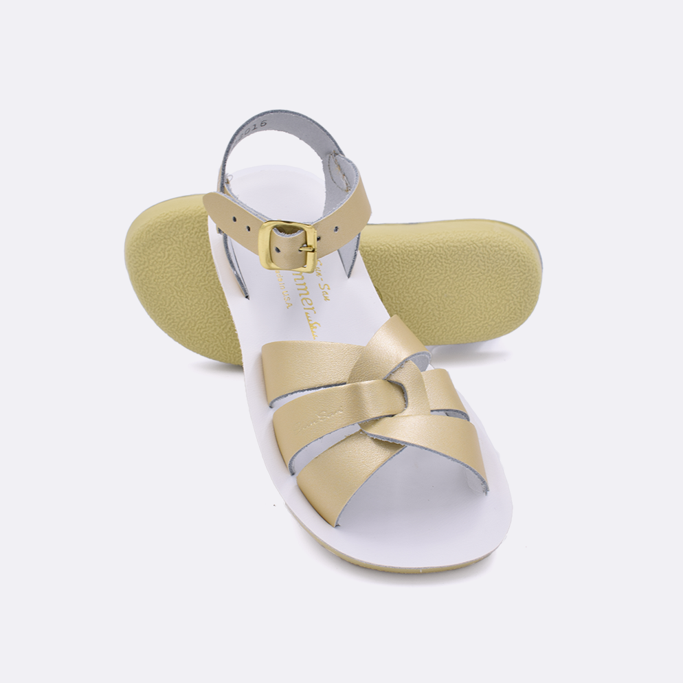 Two little kid sized 8000 Swimmer style sandals with gold straps and white insoles.  One standing with the sole facing the camera. The second is laying diagonally over the top left edge of the sole.