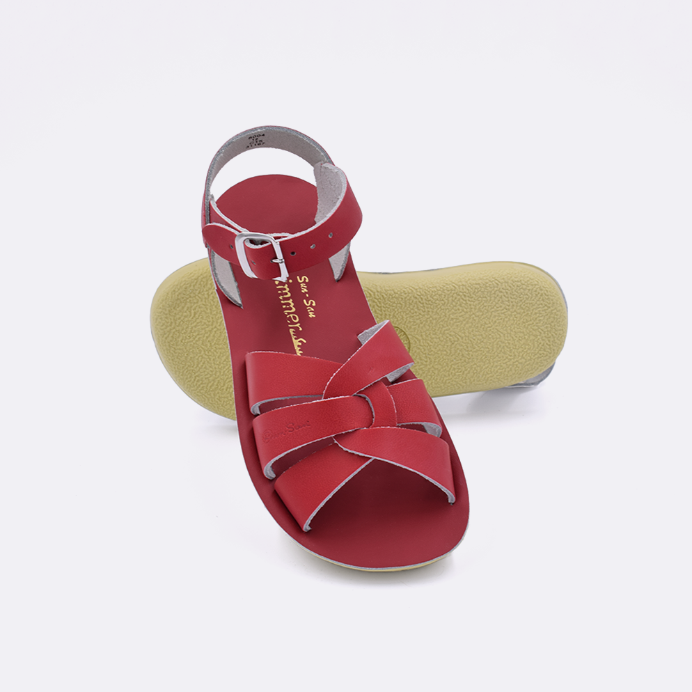 Two little kid sized 8000 Swimmer style sandals with red straps and red insoles.  One standing with the sole facing the camera. The second is laying diagonally over the top left edge of the sole.
