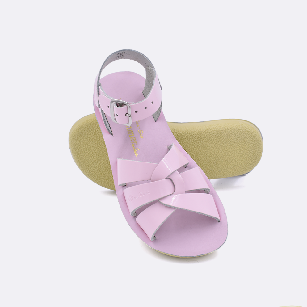Two little kid sized 8000 Swimmer style sandals with shiny pink straps and shiny pink insoles.  One standing with the sole facing the camera. The second is laying diagonally over the top left edge of the sole.