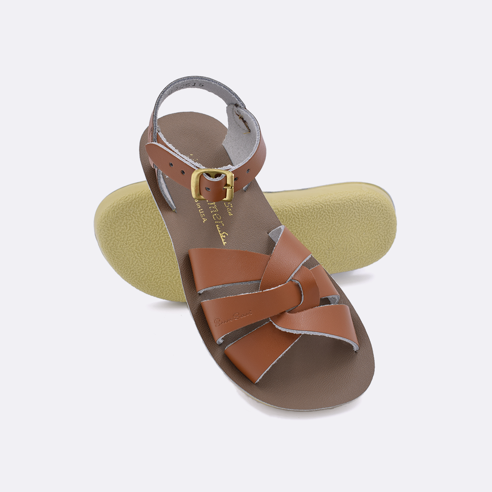Two little kid sized 8000 Swimmer style sandals with tan straps and beige insoles.  One standing with the sole facing the camera. The second is laying diagonally over the top left edge of the sole.