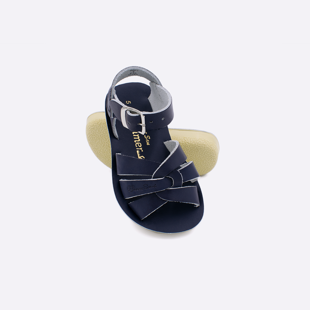 Two toddler sized 8000 Swimmer style sandals with navy straps and navy insoles.  One standing with the sole facing the camera. The second is laying diagonally over the top left edge of the sole.