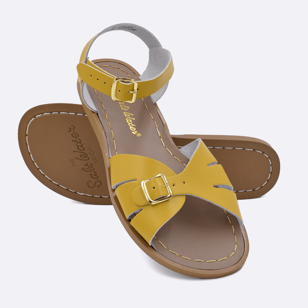 Two 900 Classic style sandals color mustard.  One standing with the sole facing the camera. The second is laying diagonally over the top left edge of the sole.	Adult Size.