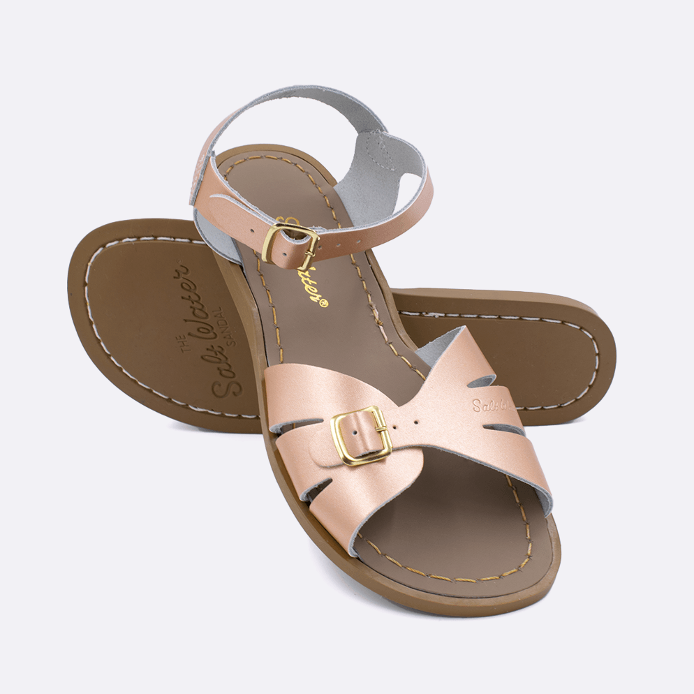Two 900 Classic style sandals color rose gold.  One standing with the sole facing the camera. The second is laying diagonally over the top left edge of the sole.	Adult Size.