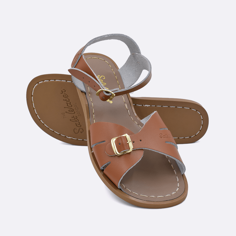 Two 900 Classic style sandals color tan.  One standing with the sole facing the camera. The second is laying diagonally over the top left edge of the sole. Adult Size