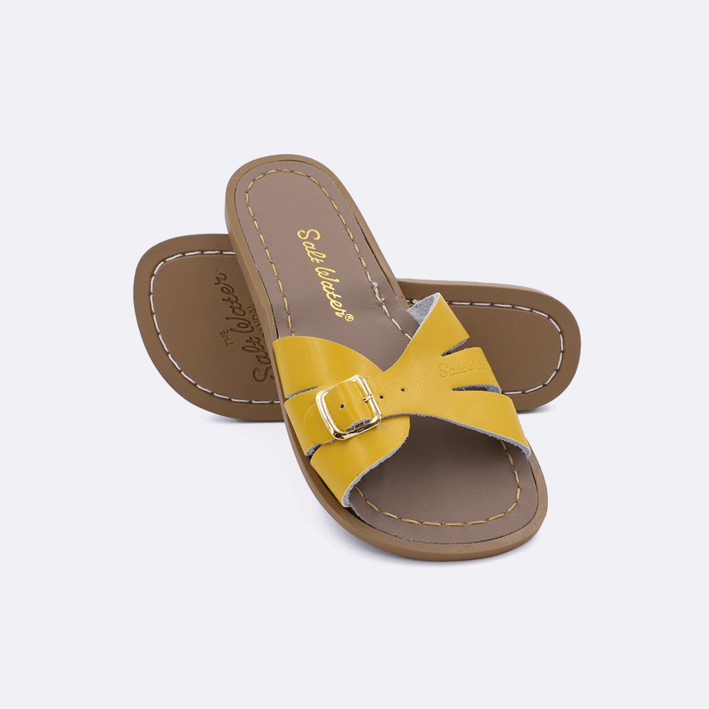 Two 9900 Classic Slide style sandals color mustard.  One standing with the sole facing the camera. The second is laying diagonally over the top left edge of the sole.	Little Kid Size.