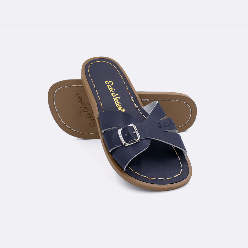 Two 9900 Classic Slide style sandals color navy.  One standing with the sole facing the camera. The second is laying diagonally over the top left edge of the sole.	Little Kid Size.
