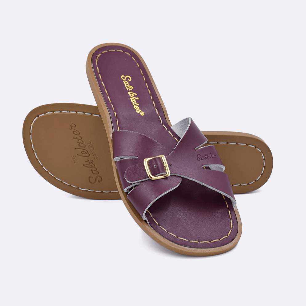 Two 9900 Classic Slide style sandals color claret.  One standing with the sole facing the camera. The second is laying diagonally over the top left edge of the sole.	Adult Size.