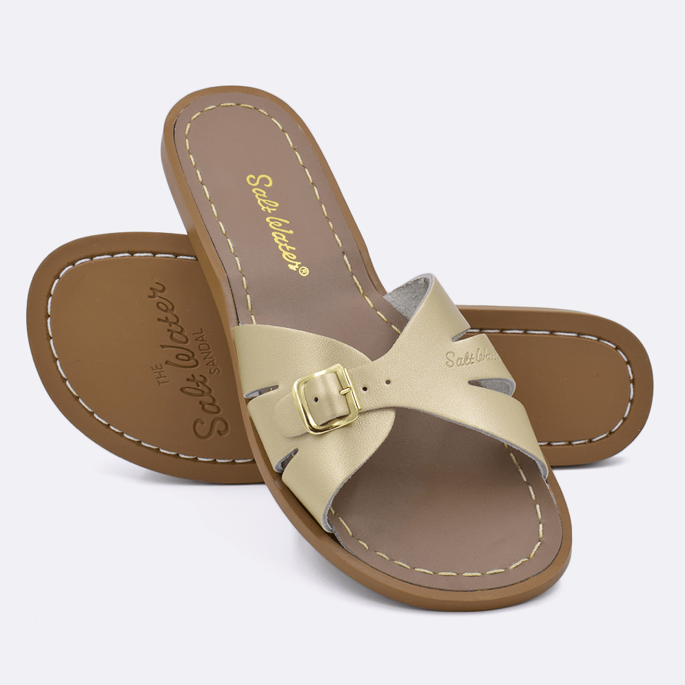 Two 9900 Classic Slide style sandals color gold.  One standing with the sole facing the camera. The second is laying diagonally over the top left edge of the sole.	Adult Size.